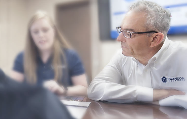 Photo of Swanson employees in a meeting room studying files on the table